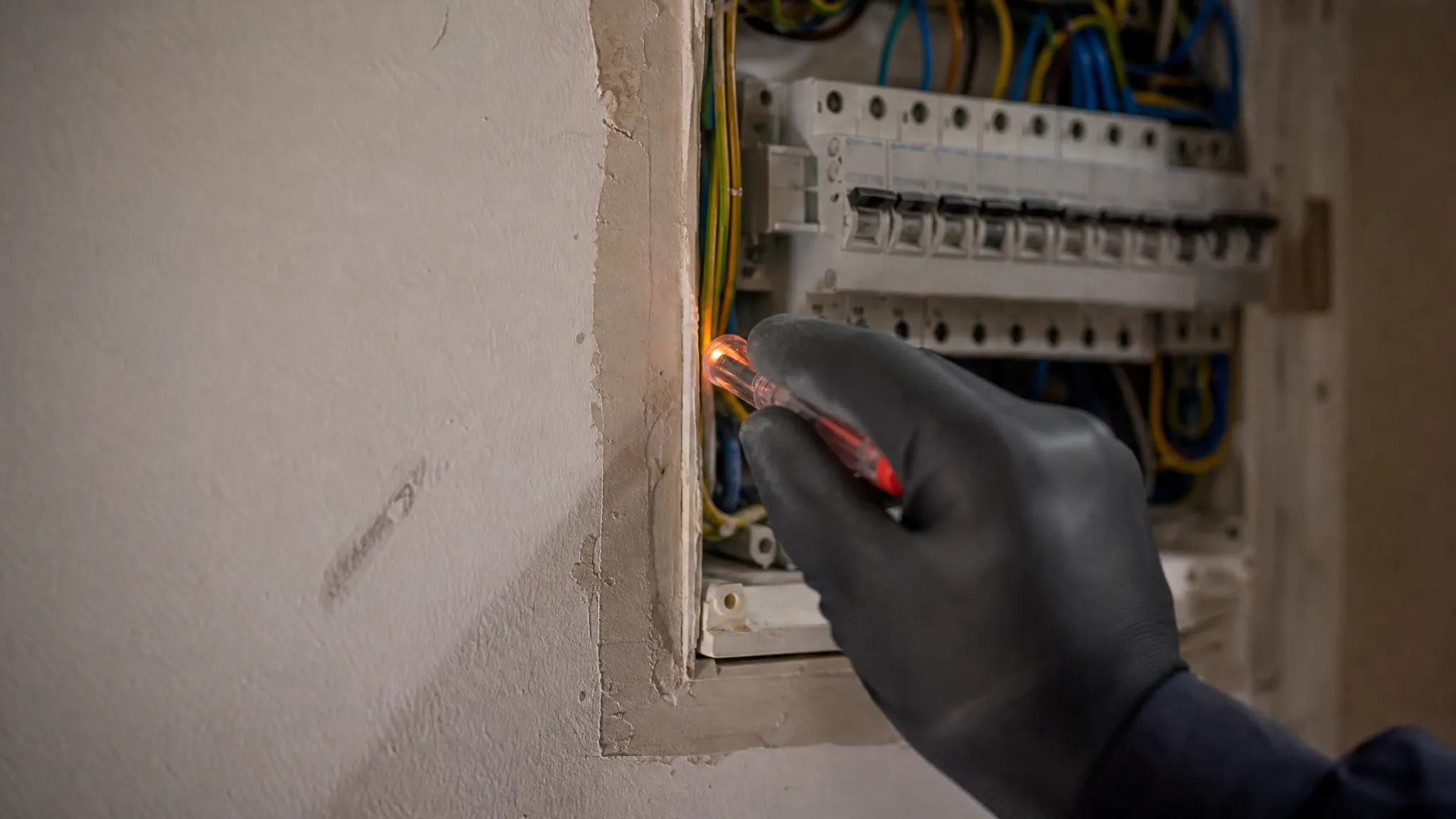 gloved hand testing an open household electrical switchboard, licensed electrician work