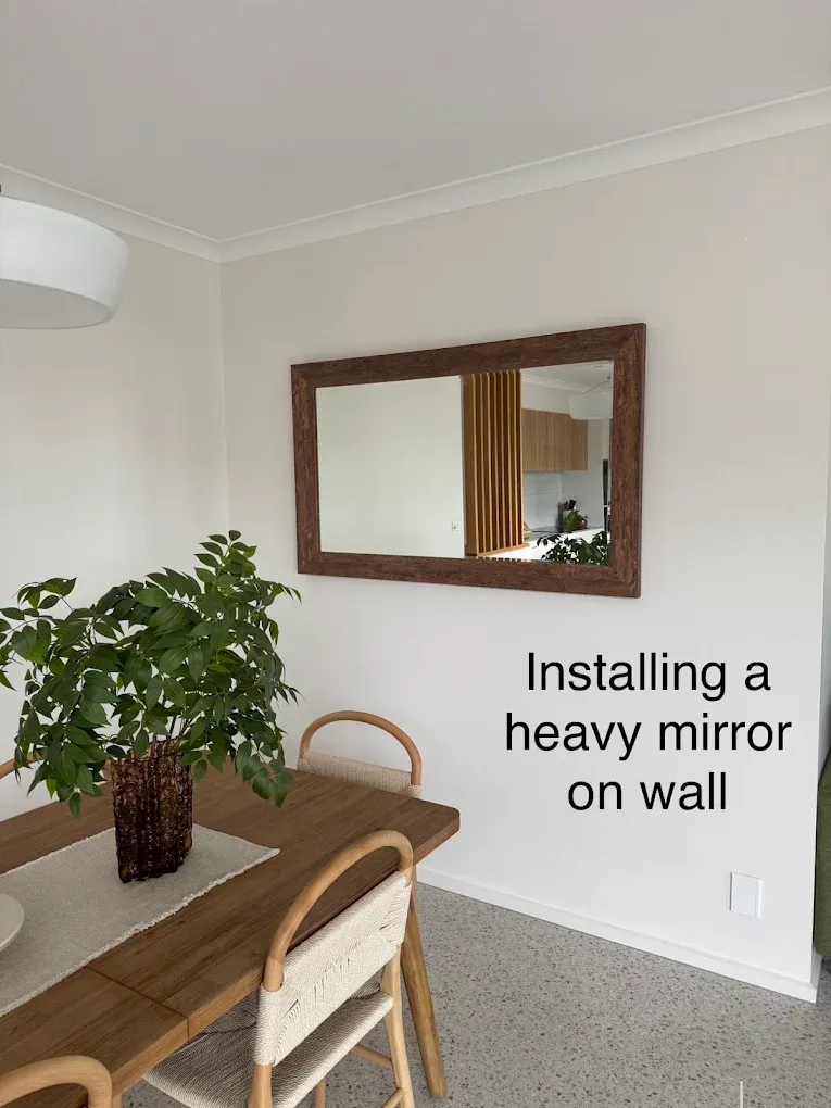 A large timber-framed mirror mounted on a dining room wall above a table, installed level and fixed for weight.