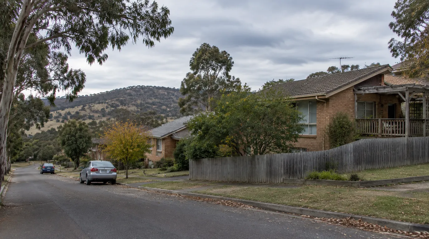 A Jerrabomberra street in New South Wales with established brick homes, timber fencing and mature garden trees below Jerrabomberra Mountain
