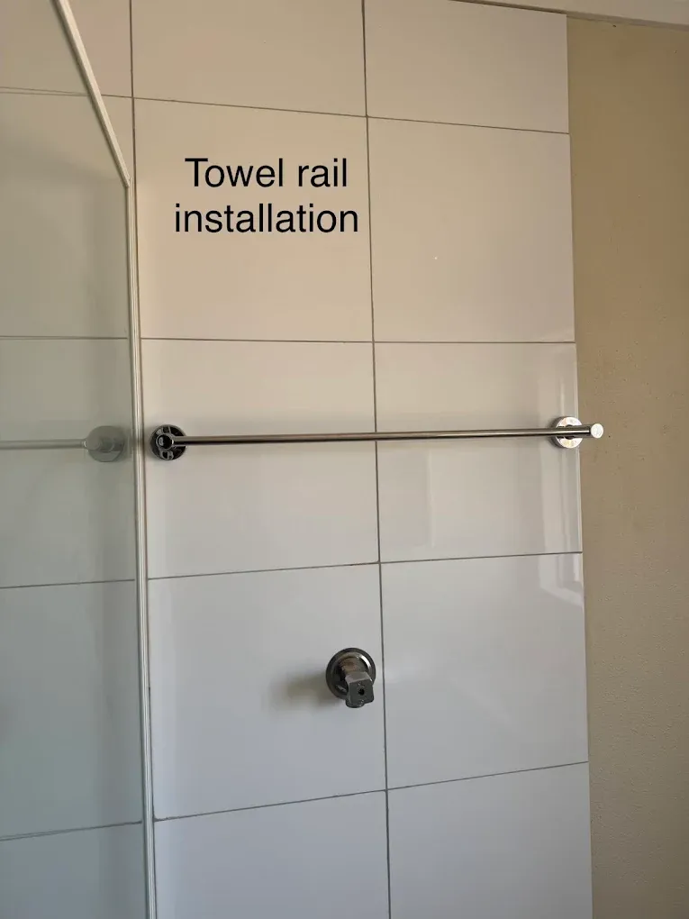 A stainless towel rail installed on a tiled bathroom wall beside a shower screen, drilled and anchored through the tile.